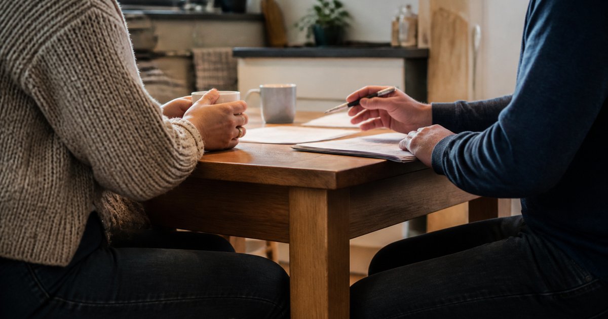Twee mensen in gesprek aan een keukentafel met papieren